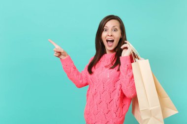Örgü pembe kazak işaret parmağı bir kenara paketleri çanta ile tutarak sürpriz genç kadın üzerinde izole mavi arka plan alışveriş sonra alımları. İnsanlar yaşam tarzı kavramı. Kopyalama alanı alay