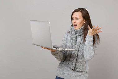 Gri duvar arka plan üzerinde izole dizüstü pc bilgisayar üzerinde çalışan çapraşık genç kadın gri kazak ve eller, yaymak eşarp. Sağlıklı yaşam, online tedavi danışmanlık, soğuk sezon kavramı