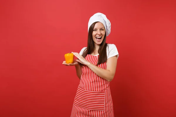 Housewife female chef cook or baker in striped apron, white t-shirt, toque chefs hat isolated on red wall background in studio. Smiling woman hold in hand yellow pepper. Mock up copy space concept