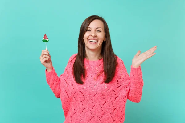 笑着穿着针织粉色毛衣的年轻女子摊开双手 拿着西瓜棒棒糖隔离在蓝色绿松石墙的背景下 工作室的肖像 人的生活方式概念 模拟复制空间 — 图库照片