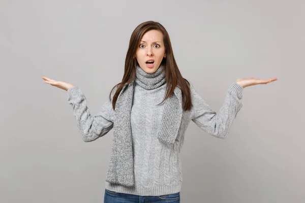 在灰色毛衣的困惑的年轻女子 围巾蔓延 指着手一边孤立在灰色背景在工作室 健康时尚的生活方式 人们的情感 寒冷的季节概念 模拟复制空间 — 图库照片