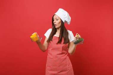 Ev hanımı kadın şef aşçı baker şapkalı izole kırmızı duvar arka plan üzerinde çizgili önlük beyaz t-shirt toque şefler. Kadın tutun sarı biber salatalık bakkal itme arabası sahte kopya alanı kavramı kadar