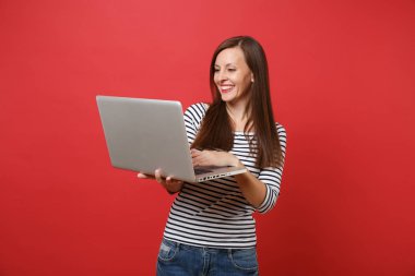 Holding, parlak kırmızı duvar arka plan üzerinde izole dizüstü pc bilgisayar üzerinde çalışan rahat çizgili kıyafetler içinde gülümseyen genç kadın portresi. İnsanlar samimi duygular, yaşam kavramı. Kopyalama alanı alay