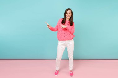 Tam uzunlukta örme gül kazaklı gülümseyen genç kadın portresi, beyaz parlak pembe mavi pastel duvar arka planda Studio izole poz pantolon. Moda yaşam tarzı kavramı. Kopyalama alanı alay