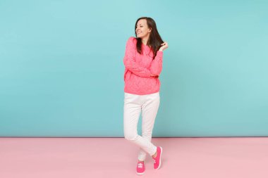 Tam uzunlukta örme gül kazaklı gülümseyen genç kadın portresi, beyaz parlak pembe mavi pastel duvar arka planda Studio izole poz pantolon. Moda yaşam tarzı kavramı. Kopyalama alanı alay