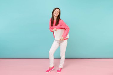 Dizüstü pc bilgisayar tutan örgü gül kazak Beyaz pantolonlu kadın portresi tam uzunlukta parlak pembe mavi pastel duvar arka planda Studio izole moda yaşam tarzı kavramı sahte kopya yer