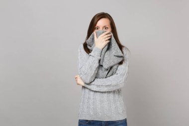 Gri süveterli gri arka plan stüdyo portre üzerinde izole eşarp ile ağız kapsayan şok genç kadın. Sağlıklı moda yaşam tarzı, insanlar samimi duygular, soğuk sezon kavramı. Kopyalama alanı alay