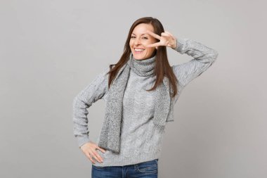 Studio gri duvar arka planda gri süveterli, zafer işareti gösterilen eşarp genç gülümseyen izole. Sağlıklı moda yaşam tarzı, insanlar samimi duygular, soğuk sezon kavramı. Kopyalama alanı alay