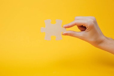 Parlak sarı duvar arka plan üzerinde izole ahşap jigsaw bulmaca parçası tutan el kırpılmış fotoğrafı kapatın. Dernek ve bağlantı kavramı. Uzay reklam sahte kopyalayın