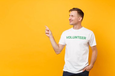 Mutlu gülümseyerek portresi genç adam beyaz t-shirt üzerinde sarı arka plan izole yazılı yazıt yeşil başlık gönüllü ile memnun. Gönüllü ücretsiz destek yardım, sadaka grace iş kavramı