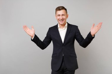 Klasik siyah takım elbise ve beyaz gömlek gri duvar arka planda Studio izole eller yayılan neşeli genç iş adamı portresi. Başarı kariyer servet iş kavramı. Kopyalama alanı alay