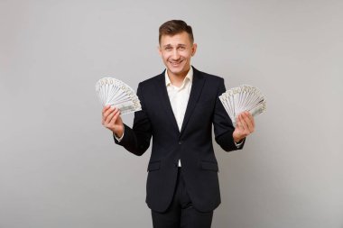 Klasik siyah elbiseli Genç iş adamı gülümseyen, gömlek holding çok dolar banknotlar, nakit para üzerinde gri arka plan izole sürü. Başarı kariyer servet iş kavramı. Kopyalama alanı alay