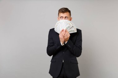 Suçlu genç iş adamı gizleme, yüz dolarlık banknot, gri arka plan üzerinde izole nakit para birçok grup ile kapsayan takım elbiseli. Başarı kariyer servet iş kavramı. Kopyalama alanı alay