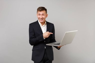 Klasik siyah takım elbise, beyaz gömlek işaret parmağı gri arka plan üzerinde izole dizüstü pc bilgisayar üzerinde neşeli genç iş adamı. Başarı kariyer servet iş kavramı. Kopyalama alanı alay