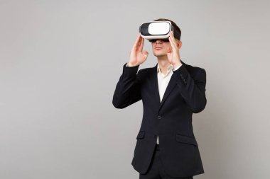 Klasik siyah takım elbise ve beyaz gömlek arıyorum Genç iş adamı, kulaklıktaki putting eller gri duvar arka planda studio izole. Başarı kariyer servet iş kavramı. Kopyalama alanı alay