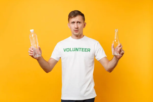Disgusted man in t-shirt volunteer hold plastic glass bottles isolated on yellow background. Voluntary free help. Environmental pollution problem. Stop nature garbage environment protection concept