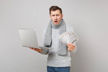 Gri süveterli dolarlık banknotlar demet çok nakit para, dizüstü pc bilgisayar gri arka plan üzerinde izole tutan eşarp çapraşık genç adam. Sağlık, online tedavi danışmanlık, soğuk sezon kavramı