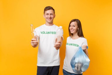 İş arkadaşları iki t-shirt sonra çöp torbası sarı arka plan üzerinde izole gönüllü. Yardım yardım yardım grace takım çalışması. Çevre kirliliği sorunu. Doğa çöp çevre korumasını durdurma