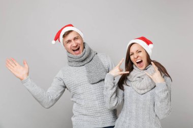 Neşeli eğlenceli çift kız adam Santa Noel şapka gri kazak eşarp gri duvar arka planda, stüdyo portre izole kırmızı. Mutlu yeni yıl 2019 kutlama tatil parti kavramı. Kopyalama alanı alay