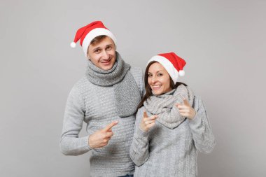 Neşeli eğlenceli çift kız adam Santa Noel şapka gri kazak eşarp gri duvar arka planda, stüdyo portre izole kırmızı. Mutlu yeni yıl 2019 kutlama tatil parti kavramı. Kopyalama alanı alay