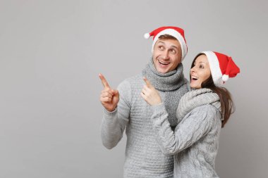 Neşeli eğlenceli çift kız adam Santa Noel şapka gri kazak eşarp gri duvar arka planda, stüdyo portre izole kırmızı. Mutlu yeni yıl 2019 kutlama tatil parti kavramı. Kopyalama alanı alay