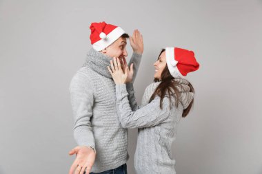 Neşeli eğlenceli çift kız adam Santa Noel şapka gri kazak eşarp gri duvar arka planda, stüdyo portre izole kırmızı. Mutlu yeni yıl 2019 kutlama tatil parti kavramı. Kopyalama alanı alay