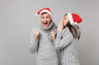 Neşeli eğlenceli çift kız adam Santa Noel şapka gri kazak eşarp gri duvar arka planda, stüdyo portre izole kırmızı. Mutlu yeni yıl 2019 kutlama tatil parti kavramı. Kopyalama alanı alay