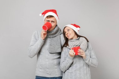 Kırmızı Santa Noel şapka gri kazak eşarp eğlenceli çift kız adam gri duvar arka planda, stüdyo portre izole çay bardak tutun. Mutlu yeni yıl 2019 tatil parti kavramı. Kopyalama alanı alay