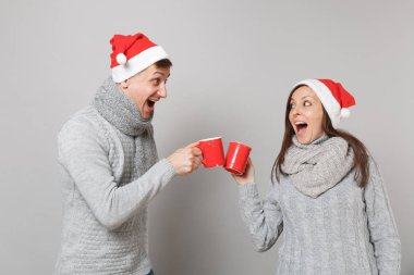 Kırmızı Santa Noel şapka gri kazak eşarp eğlenceli çift kız adam gri duvar arka planda, stüdyo portre izole çay bardak tutun. Mutlu yeni yıl 2019 tatil parti kavramı. Kopyalama alanı alay