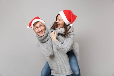 Neşeli eğlenceli çift kız adam Santa Noel şapka gri kazak eşarp gri duvar arka planda, stüdyo portre izole kırmızı. Mutlu yeni yıl 2019 kutlama tatil parti kavramı. Kopyalama alanı alay
