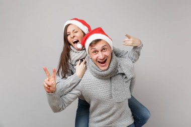 Neşeli eğlenceli çift kız adam Santa Noel şapka gri kazak eşarp gri duvar arka planda, stüdyo portre izole kırmızı. Mutlu yeni yıl 2019 kutlama tatil parti kavramı. Kopyalama alanı alay