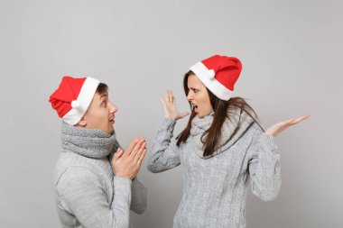 Neşeli eğlenceli çift kız adam Santa Noel şapka gri kazak eşarp gri duvar arka planda, stüdyo portre izole kırmızı. Mutlu yeni yıl 2019 kutlama tatil parti kavramı. Kopyalama alanı alay