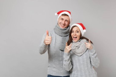 Neşeli eğlenceli çift kız adam Santa Noel şapka gri kazak eşarp gri duvar arka planda, stüdyo portre izole kırmızı. Mutlu yeni yıl 2019 kutlama tatil parti kavramı. Kopyalama alanı alay