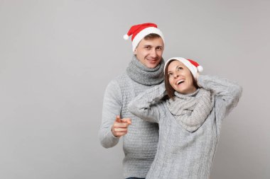 Neşeli eğlenceli çift kız adam Santa Noel şapka gri kazak eşarp gri duvar arka planda, stüdyo portre izole kırmızı. Mutlu yeni yıl 2019 kutlama tatil parti kavramı. Kopyalama alanı alay