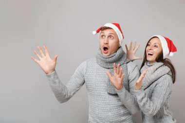 Neşeli eğlenceli çift kız adam Santa Noel şapka gri kazak eşarp gri duvar arka planda, stüdyo portre izole kırmızı. Mutlu yeni yıl 2019 kutlama tatil parti kavramı. Kopyalama alanı alay