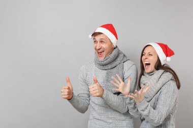 Neşeli eğlenceli çift kız adam Santa Noel şapka gri kazak eşarp gri duvar arka planda, stüdyo portre izole kırmızı. Mutlu yeni yıl 2019 kutlama tatil parti kavramı. Kopyalama alanı alay