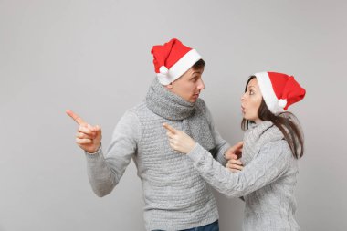 Neşeli eğlenceli çift kız adam Santa Noel şapka gri kazak eşarp gri duvar arka planda, stüdyo portre izole kırmızı. Mutlu yeni yıl 2019 kutlama tatil parti kavramı. Kopyalama alanı alay