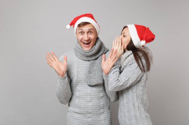 Neşeli eğlenceli çift kız adam Santa Noel şapka gri kazak eşarp gri duvar arka planda, stüdyo portre izole kırmızı. Mutlu yeni yıl 2019 kutlama tatil parti kavramı. Kopyalama alanı alay