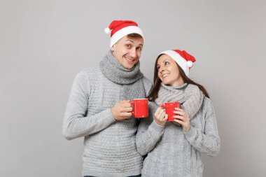 Kırmızı Santa Noel şapka gri kazak eşarp eğlenceli çift kız adam gri duvar arka planda, stüdyo portre izole çay bardak tutun. Mutlu yeni yıl 2019 tatil parti kavramı. Kopyalama alanı alay
