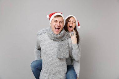Neşeli eğlenceli çift kız adam Santa Noel şapka gri kazak eşarp gri duvar arka planda, stüdyo portre izole kırmızı. Mutlu yeni yıl 2019 kutlama tatil parti kavramı. Kopyalama alanı alay