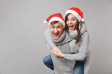 Neşeli eğlenceli çift kız adam Santa Noel şapka gri kazak eşarp gri duvar arka planda, stüdyo portre izole kırmızı. Mutlu yeni yıl 2019 kutlama tatil parti kavramı. Kopyalama alanı alay