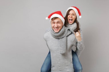 Neşeli eğlenceli çift kız adam Santa Noel şapka gri kazak eşarp gri duvar arka planda, stüdyo portre izole kırmızı. Mutlu yeni yıl 2019 kutlama tatil parti kavramı. Kopyalama alanı alay