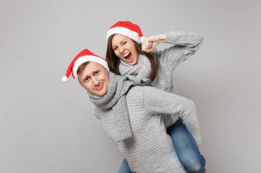 Neşeli eğlenceli çift kız adam Santa Noel şapka gri kazak eşarp gri duvar arka planda, stüdyo portre izole kırmızı. Mutlu yeni yıl 2019 kutlama tatil parti kavramı. Kopyalama alanı alay