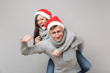 Neşeli eğlenceli çift kız adam Santa Noel şapka gri kazak eşarp gri duvar arka planda, stüdyo portre izole kırmızı. Mutlu yeni yıl 2019 kutlama tatil parti kavramı. Kopyalama alanı alay
