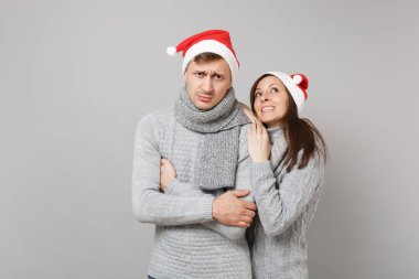 Neşeli eğlenceli çift kız adam Santa Noel şapka gri kazak eşarp gri duvar arka planda, stüdyo portre izole kırmızı. Mutlu yeni yıl 2019 kutlama tatil parti kavramı. Kopyalama alanı alay