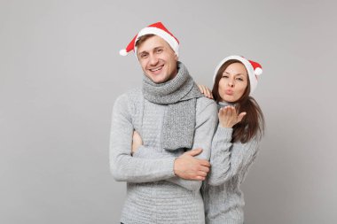 Neşeli eğlenceli çift kız adam Santa Noel şapka gri kazak eşarp gri duvar arka planda, stüdyo portre izole kırmızı. Mutlu yeni yıl 2019 kutlama tatil parti kavramı. Kopyalama alanı alay