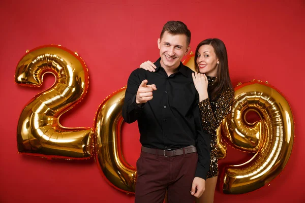 Couple guy girl in shiny glitter dress, black shirt celebrating holiday party isolated on bright red wall background golden numbers air balloons studio portrait. Happy New Year 2019 Christmas concept