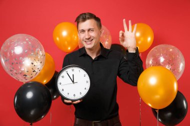 Yuvarlak holding neşeli genç adam Ok işareti, gösterilen siyah klasik gömlek parlak kırmızı arka plan hava balonları saat. Dünya Kadınlar günü, mutlu yeni yıl, Doğum günü mockup tatil parti konsept