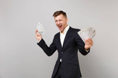 Dolar banknotlar demet çok gri arka plan üzerinde izole nakit para tutan klasik siyah takım elbise çığlık içinde mutlu genç iş adamı. Başarı kariyer servet iş kavramı. Kopyalama alanı alay