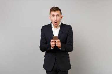 Şok genç iş adamı tutmak ağzı açık geniş, cep telefonunuzun sms mesajı yazarak gri arka plan üzerinde izole sürpriz arıyor. Başarı kariyer servet iş kavramı. Kopyalama alanı alay
